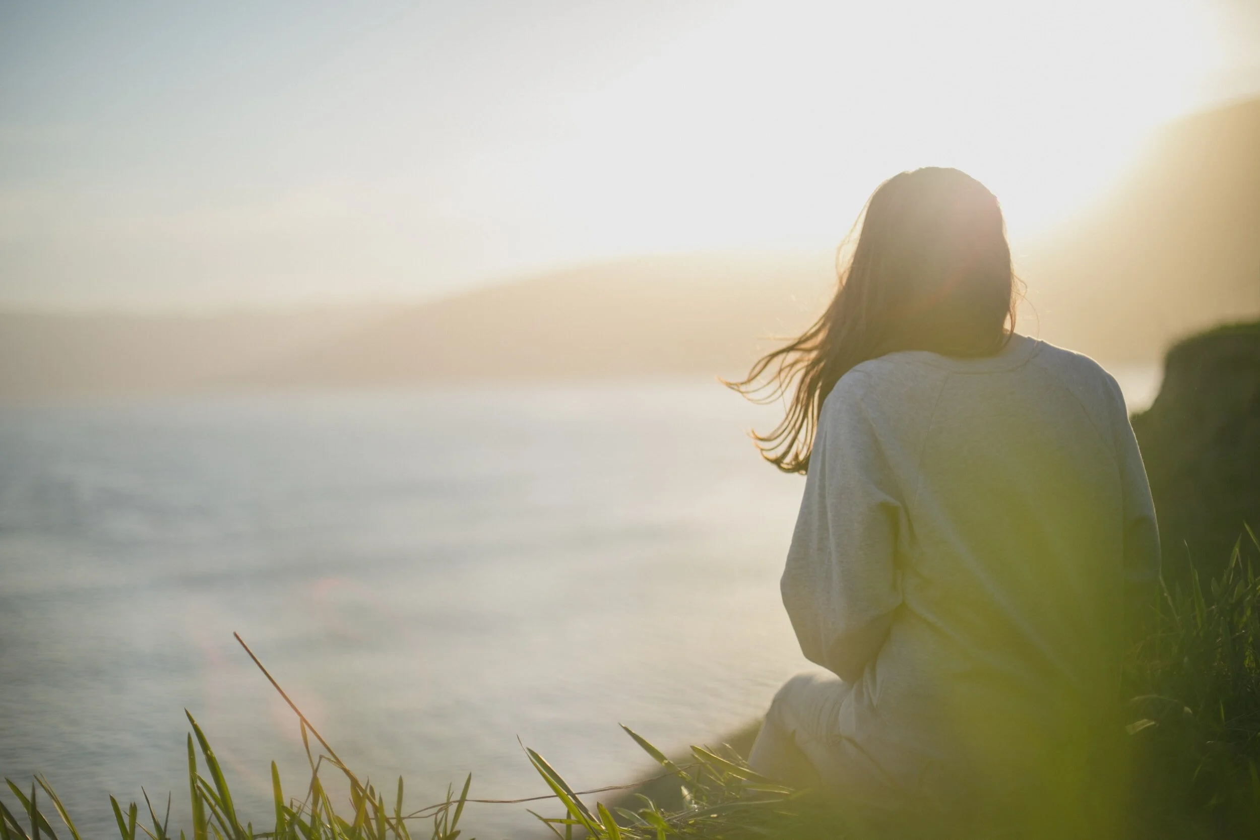 A woman sitting peacefully beside the water at sunset